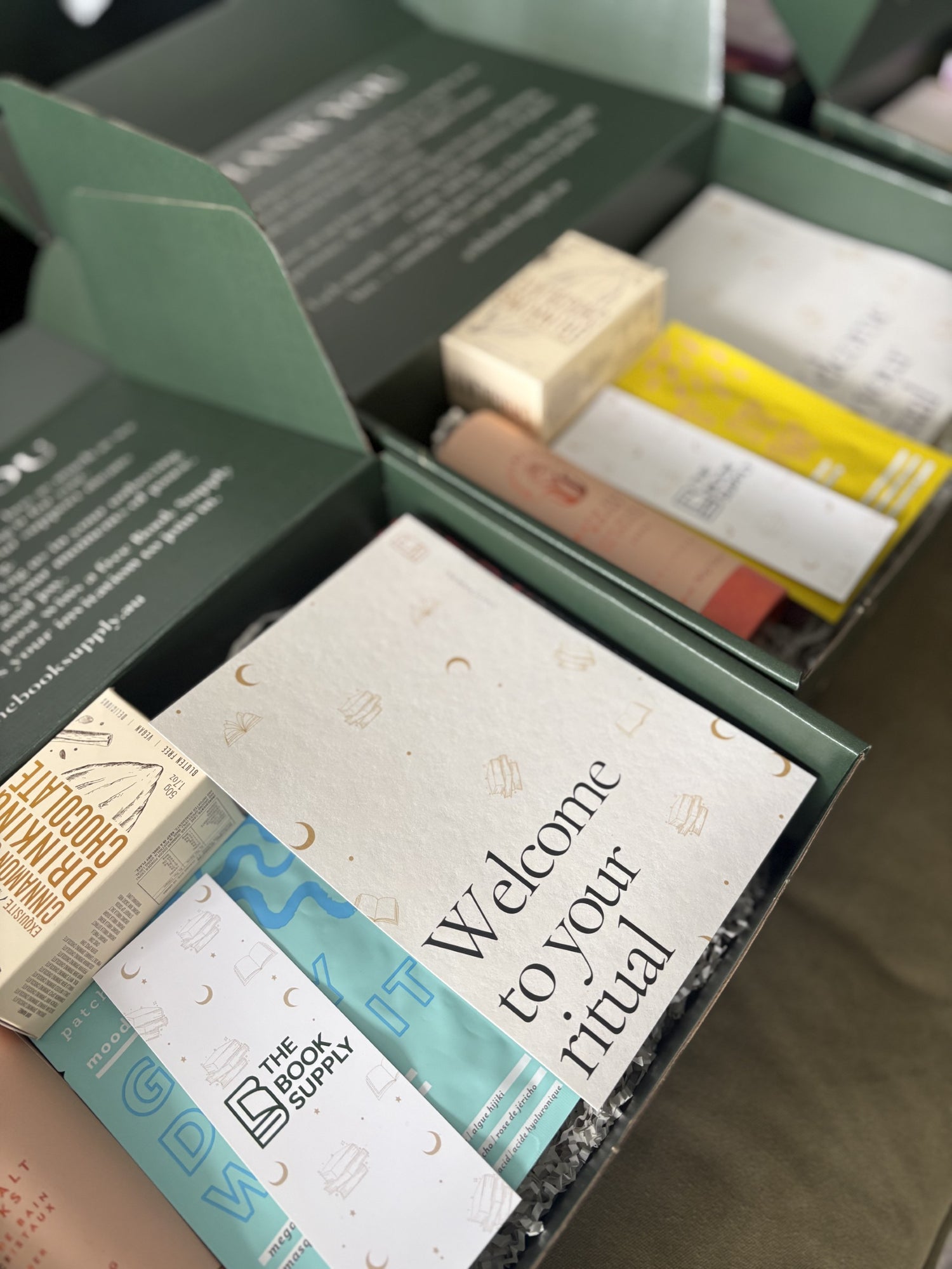 Open box containing items with a 'Welcome to your ritual' card, featuring The Book Supply branding.